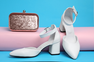 Stylish white female shoes and bag on light blue background