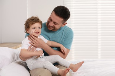 Photo of Father applying ointment onto his son`s cheek on bed at home. Space for text