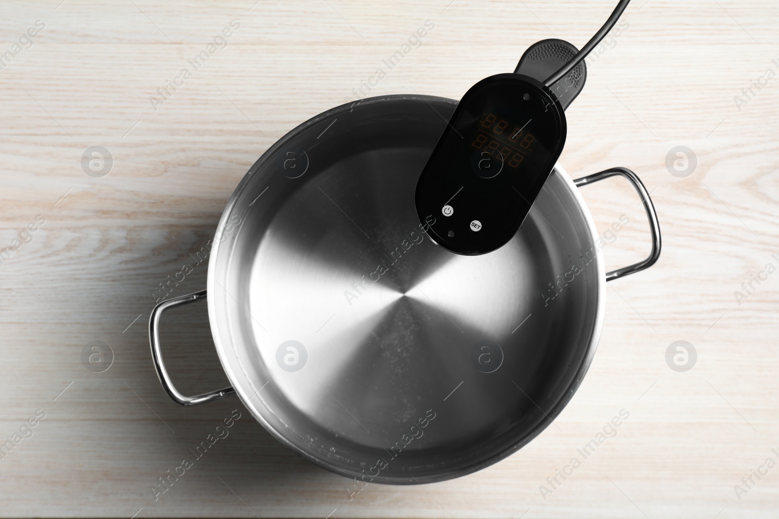 Photo of Thermal immersion circulator in pot on white wooden table, top view. Sous vide cooker