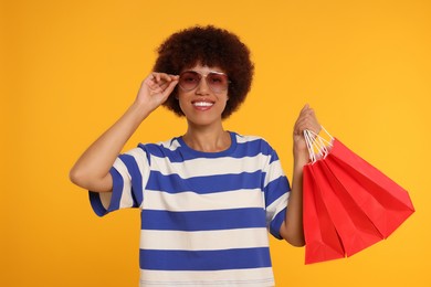 Photo of Happy young woman in stylish sunglasses with shopping bags on orange background