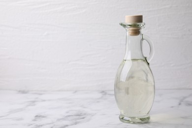 Vinegar in glass jug on white marble table, space for text