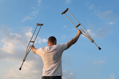 Photo of Man raising hands with underarm crutches up to sky outdoors, back view. Healing miracle