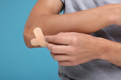 Man putting sticking plasters onto elbow on light blue background, closeup