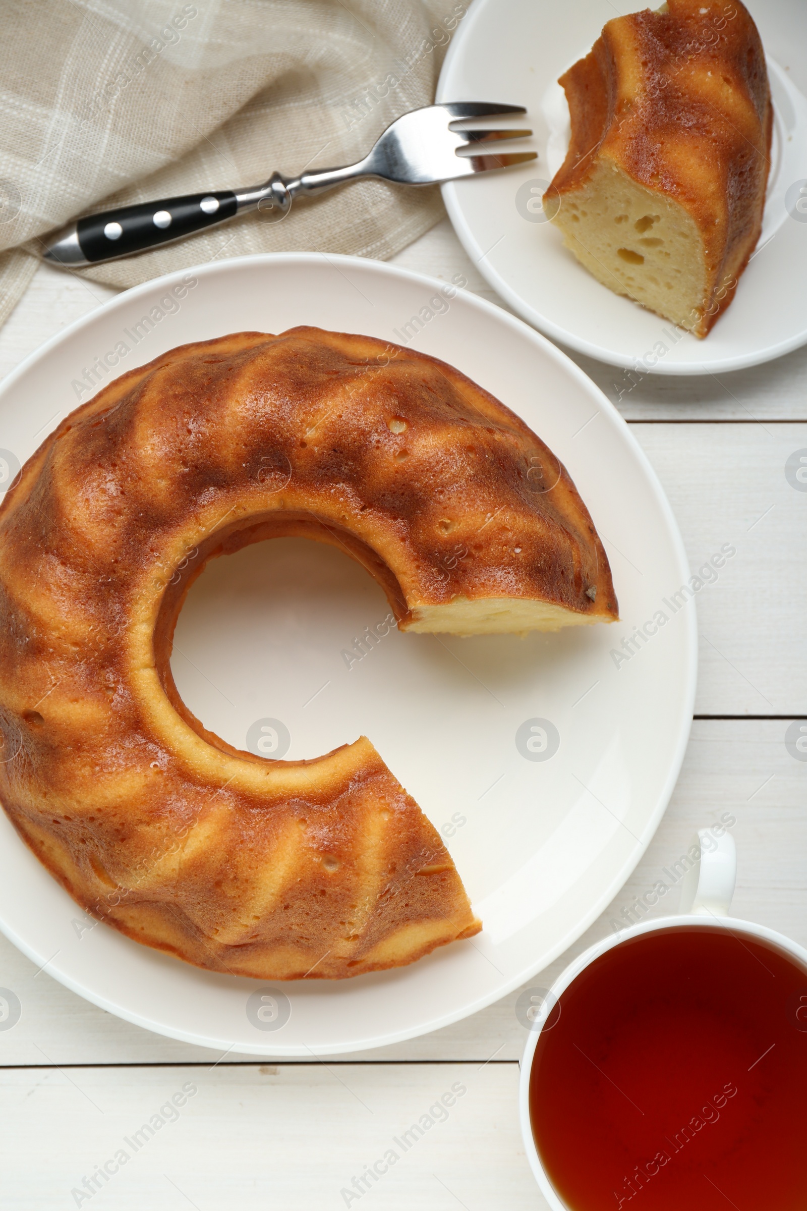 Photo of Delicious homemade yogurt cake and cup tea on white wooden table, flat lay