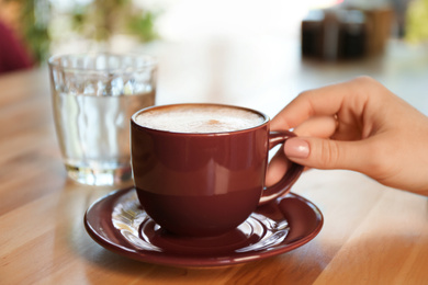 Woman with aromatic coffee at table in cafe, closeup