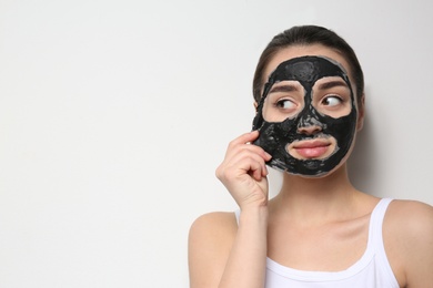 Photo of Beautiful young woman removing black mask from her face on white background. Space for text