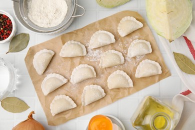 Raw dumplings (varenyky) with tasty filling and cut cabbage on white tiled table, flat lay