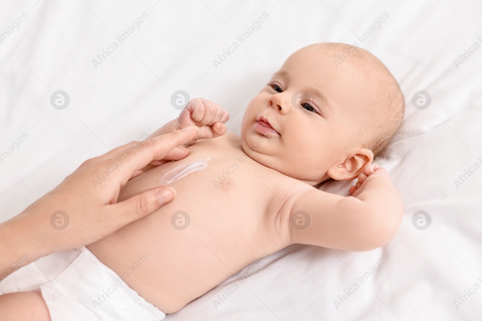 Photo of Woman applying body cream onto baby`s skin on bed, closeup