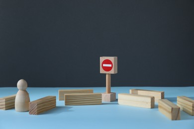 Photo of Overcoming barries for development and success. Wooden human figure movement blocked by road Stop sign on light blue surface