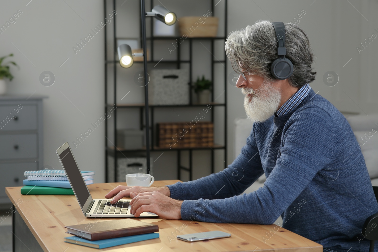 Photo of Middle aged man with laptop and headphones learning at table indoors