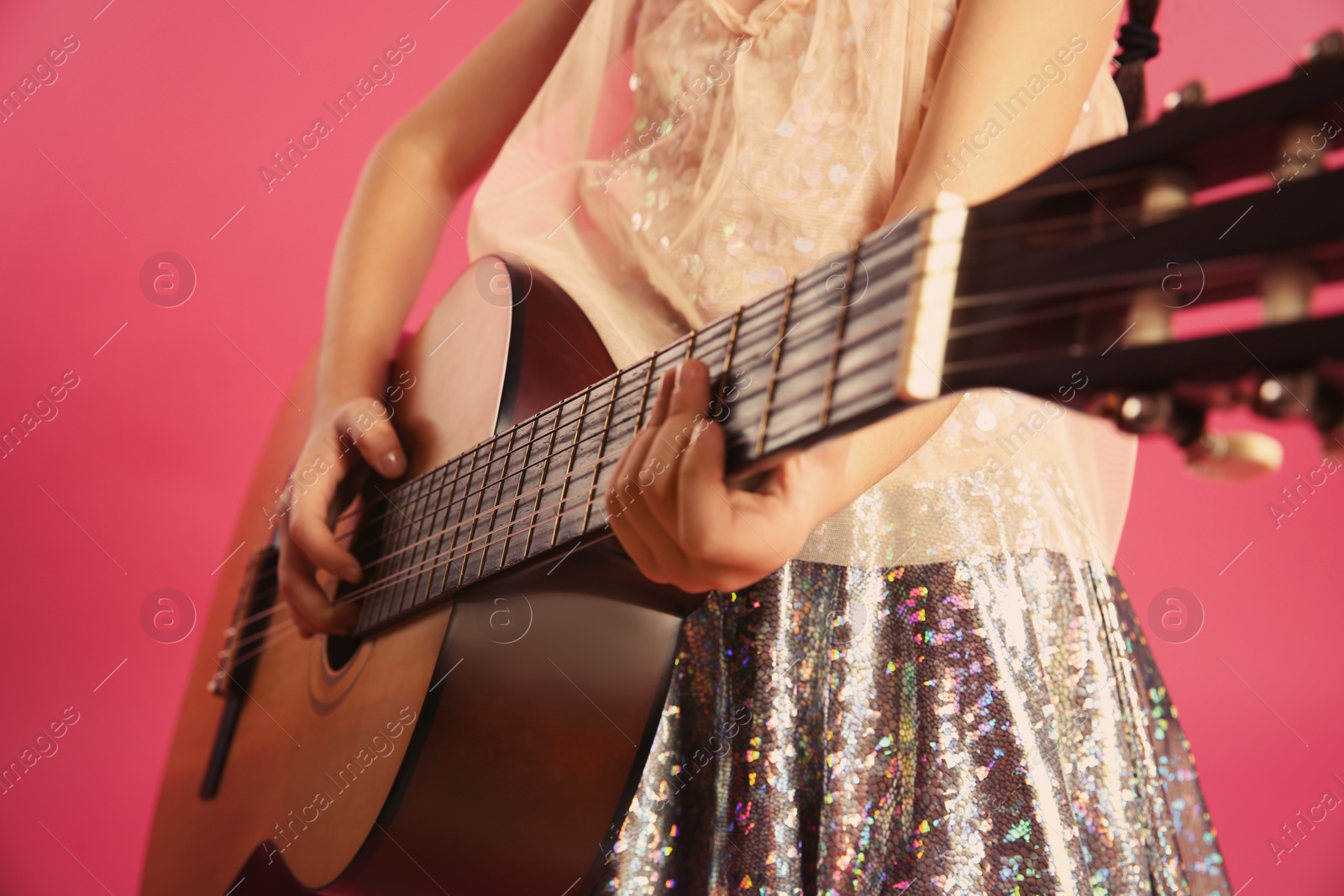 Photo of Little girl playing wooden guitar on color background, closeup