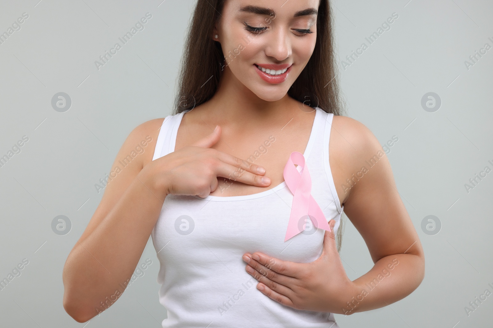 Photo of Beautiful young woman with pink ribbon on light grey background. Breast cancer awareness