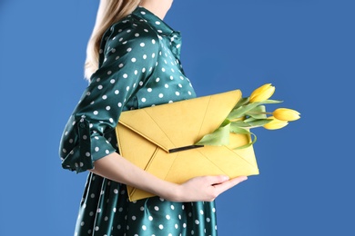 Photo of Woman holding elegant clutch with spring flowers on blue background, closeup