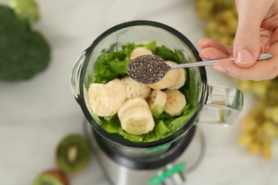 Photo of Man adding chia seeds into blender with ingredients for smoothie at table, above view