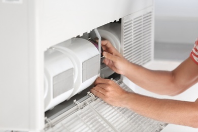 Photo of Young man fixing air conditioner at home, closeup