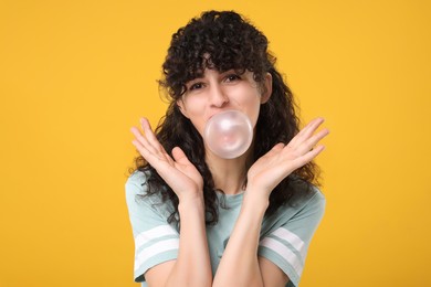 Photo of Beautiful young woman blowing bubble gum on orange background