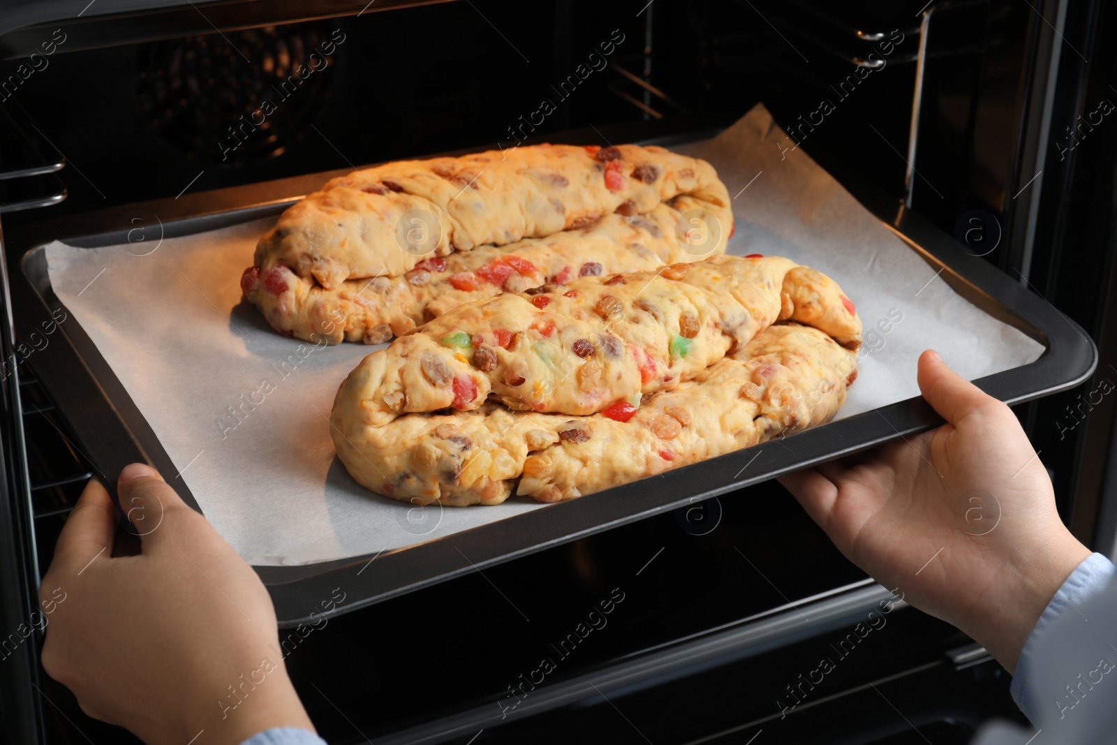 Photo of Woman putting baking tray with raw homemade Stollens into oven, closeup. Traditional German Christmas bread