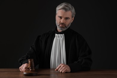 Judge with gavel sitting at wooden table against black background