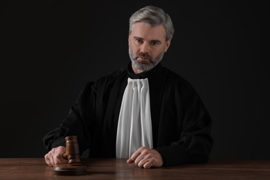 Photo of Judge with gavel sitting at wooden table against black background