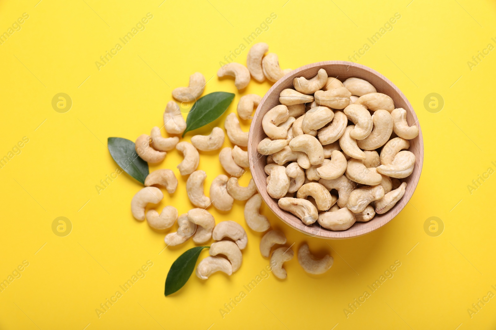 Photo of Tasty cashew nuts and green leaves on yellow background, top view