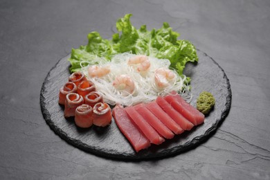 Photo of Sashimi set (raw tuna, salmon slices and shrimps) served with funchosa, lettuce and vasabi on dark table