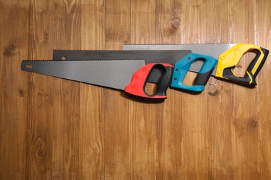 Photo of Saws with colorful handles on wooden background, flat lay. Space for text