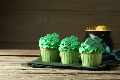 St. Patrick's day party. Tasty cupcakes with clover leaf toppers and green cream on wooden table, closeup. Space for text