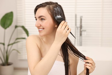 Photo of Young woman applying hair mask in bathroom