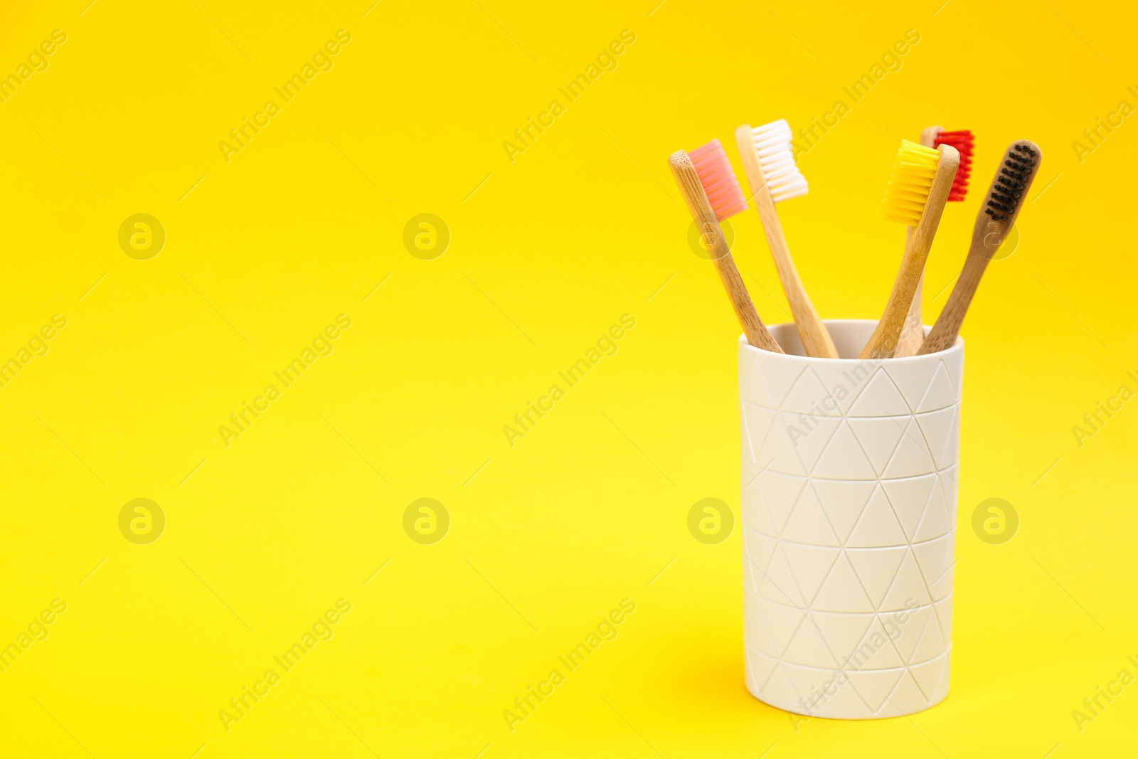 Photo of Toothbrushes made of bamboo in holder on yellow background. Space for text