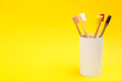 Toothbrushes made of bamboo in holder on yellow background. Space for text