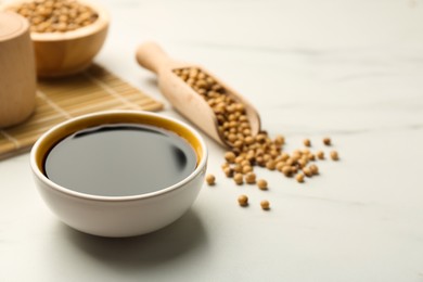 Soy sauce in bowl and soybeans on white table. Space for text