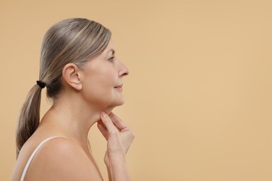 Beautiful woman touching her neck on beige background, space for text