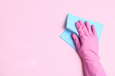 Photo of Person in rubber glove with rag on light pink background, closeup of hand. Space for text