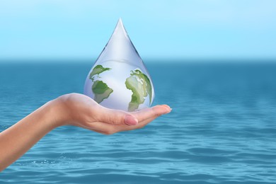 Image of Woman holding icon of Earth in drop near ocean, closeup. Water save concept