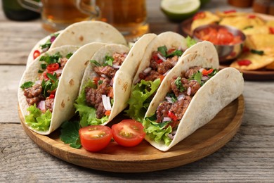 Photo of Delicious tacos with meat and vegetables on wooden table, closeup