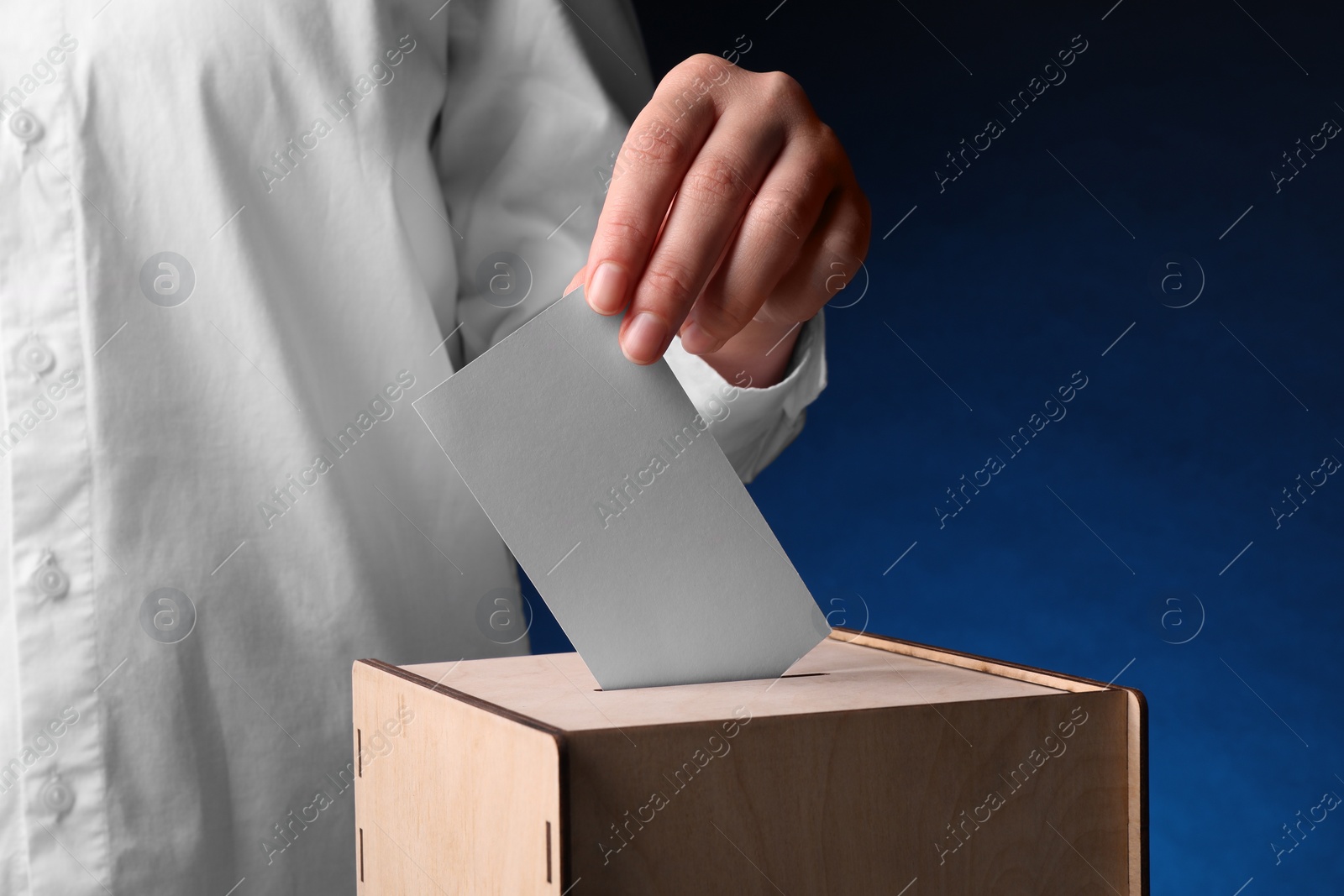 Photo of Woman putting her vote into ballot box on dark blue background, closeup