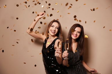 Beautiful women with glasses of champagne and confetti on color background