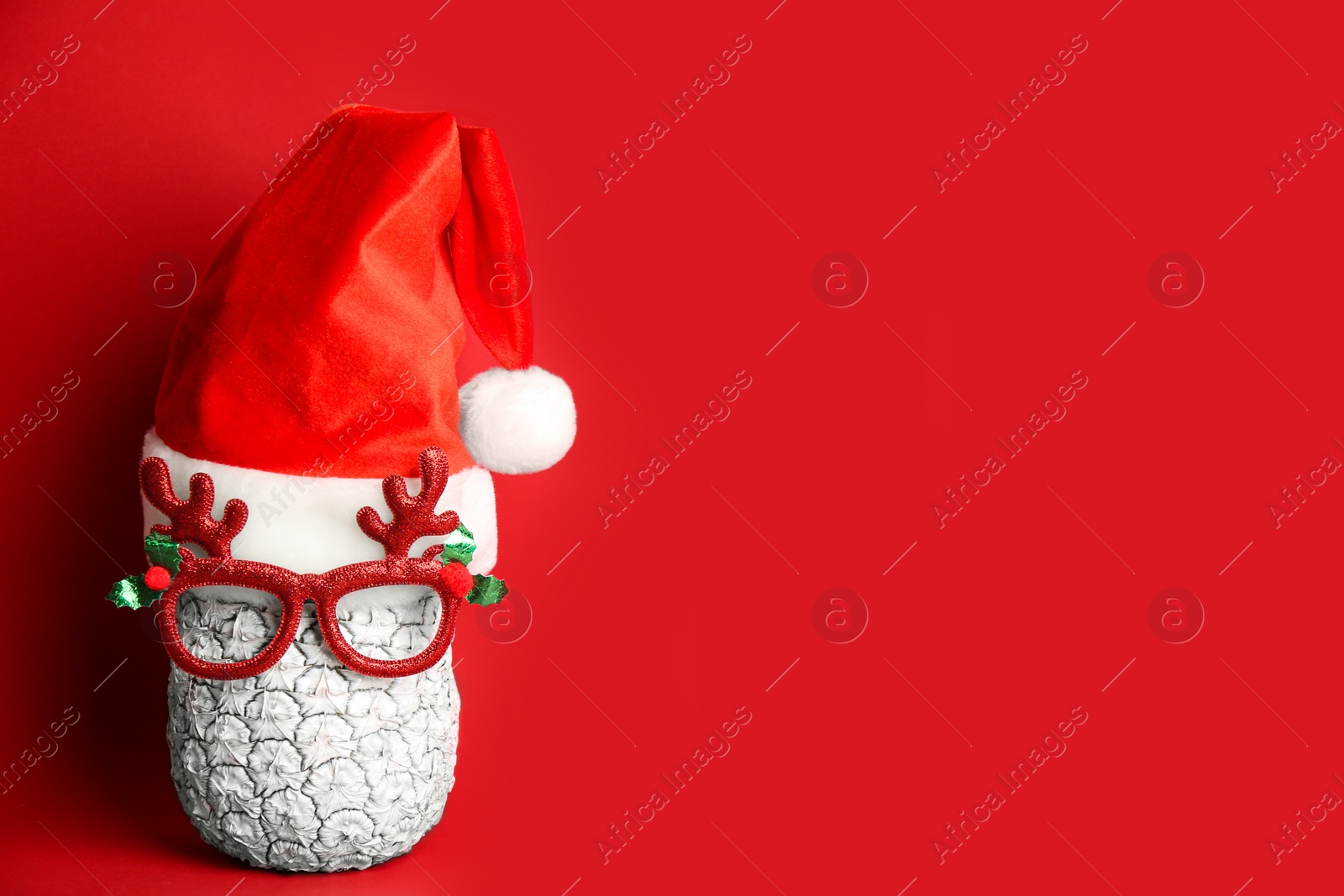 Photo of Pineapple with party glasses and Santa hat on red background, space for text. Creative concept