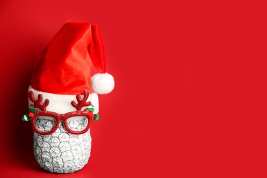 Pineapple with party glasses and Santa hat on red background, space for text. Creative concept