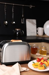 Photo of Toaster with roasted bread, tea and sandwiches on wooden table in kitchen. Tasty breakfast