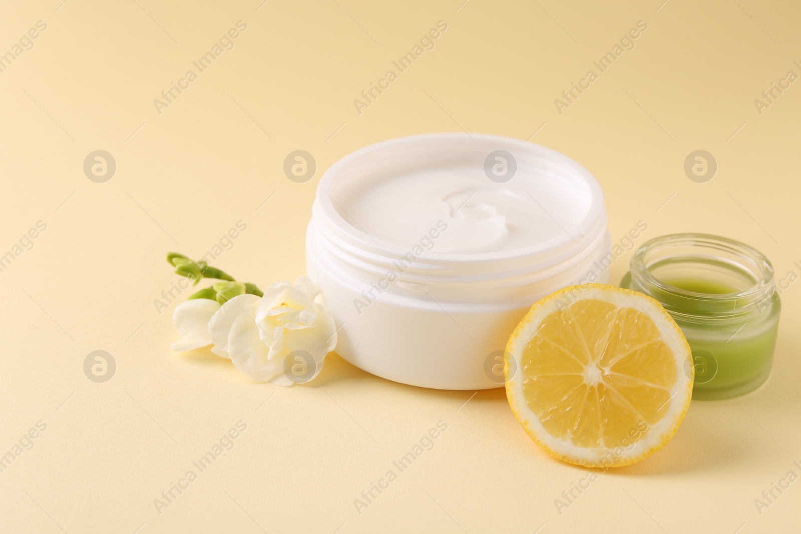 Photo of Moisturizing cream in open jars, lemon and freesia flower on beige background. Body care products