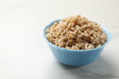 Photo of Delicious pearl barley in bowl on white marble table, closeup. Space for text