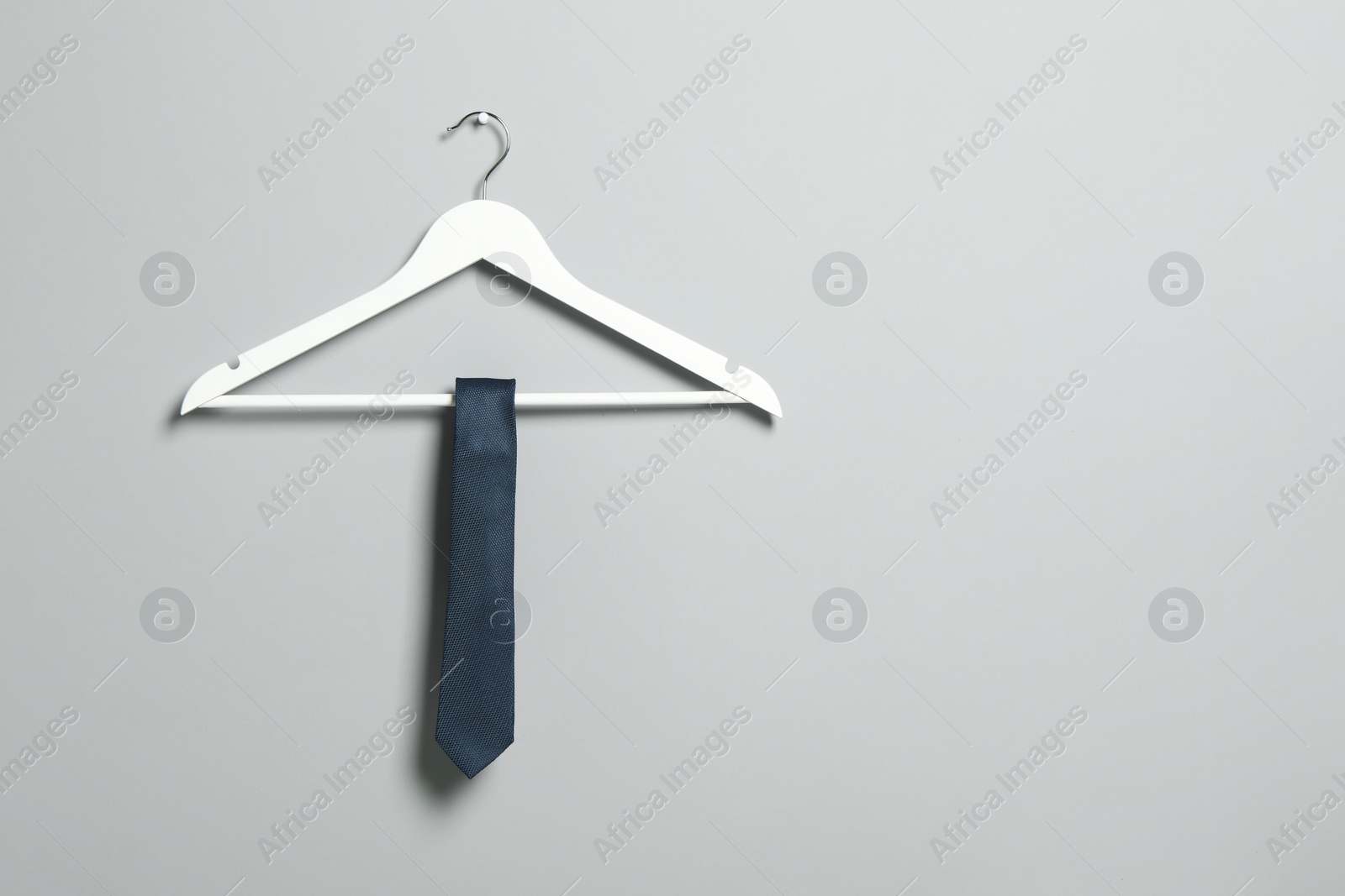 Photo of Hanger with blue necktie on light grey wall. Space for text