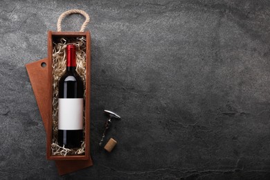 Photo of Bottle of wine in wooden box, cork and corkscrew on dark textured table, flat lay. Space for text