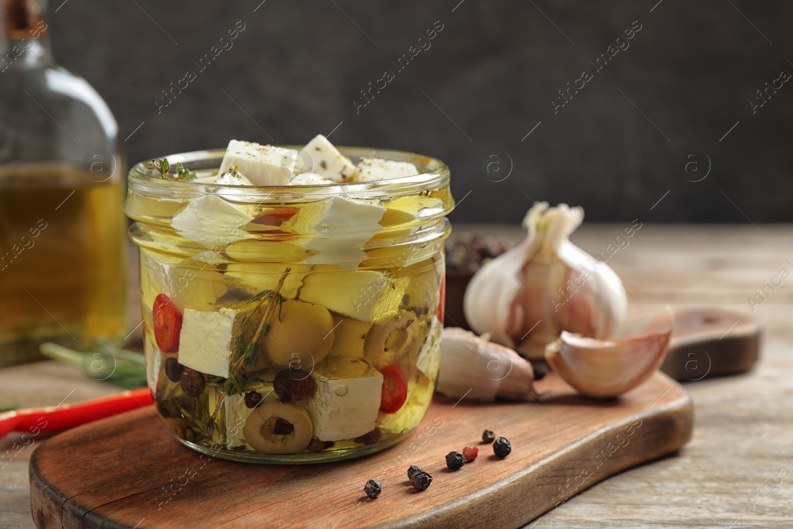 Photo of Glass jar of marinated feta cheese on wooden table