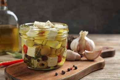 Photo of Glass jar of marinated feta cheese on wooden table