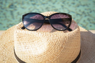 Photo of Stylish hat and sunglasses near outdoor swimming pool on sunny day, closeup