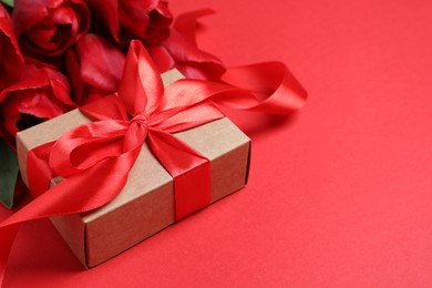 Photo of Beautiful gift box with bow and tulip flowers on red background, closeup. Space for text
