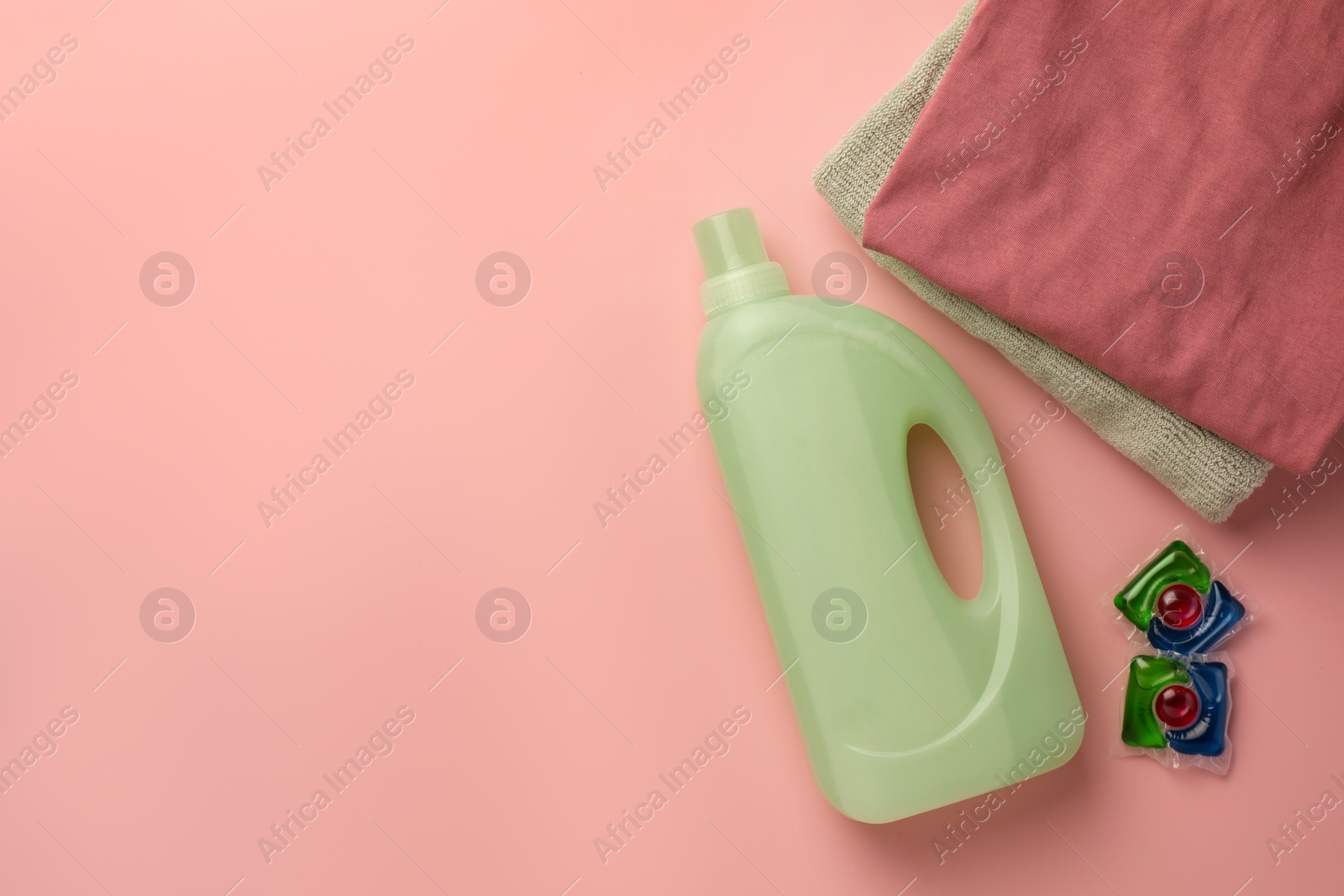 Bottle of fabric softener, stacked clean clothes and laundry capsules on pink background, flat lay. Space for text Photo of Bottle of fabric softener, stacked clean clothes and laundry capsules on pink background, flat lay. Space for text