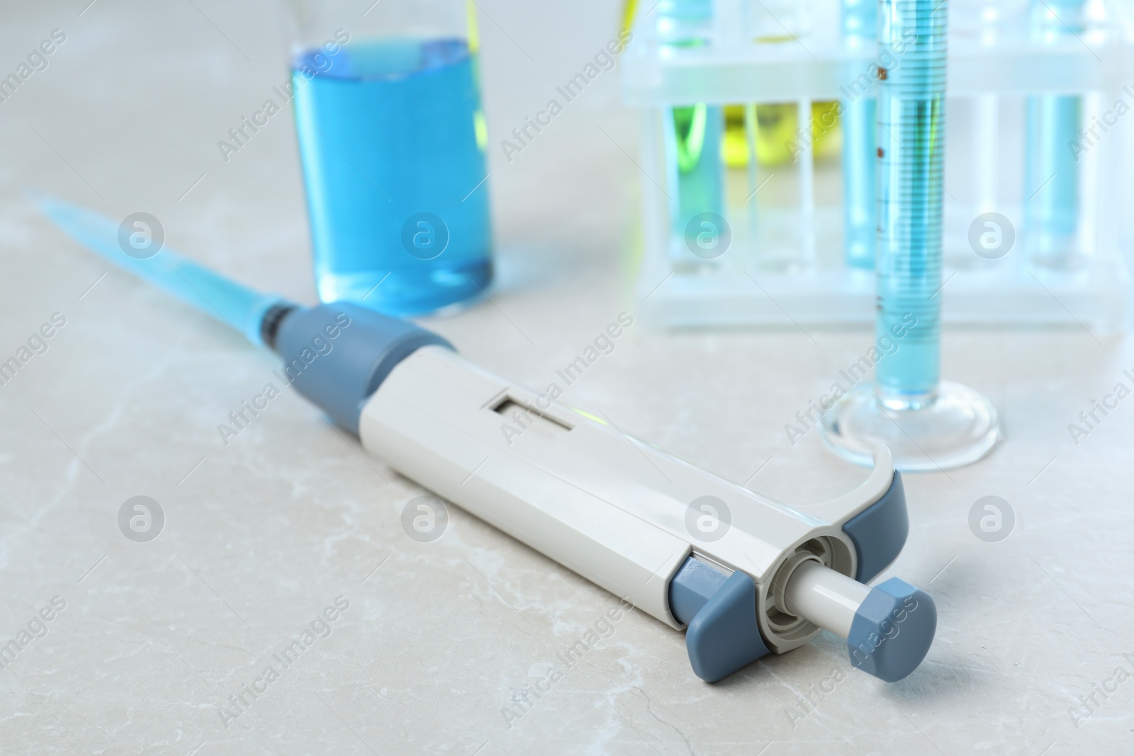 Photo of Laboratory analysis. Micropipette and different glassware with liquids on light grey marble table, closeup